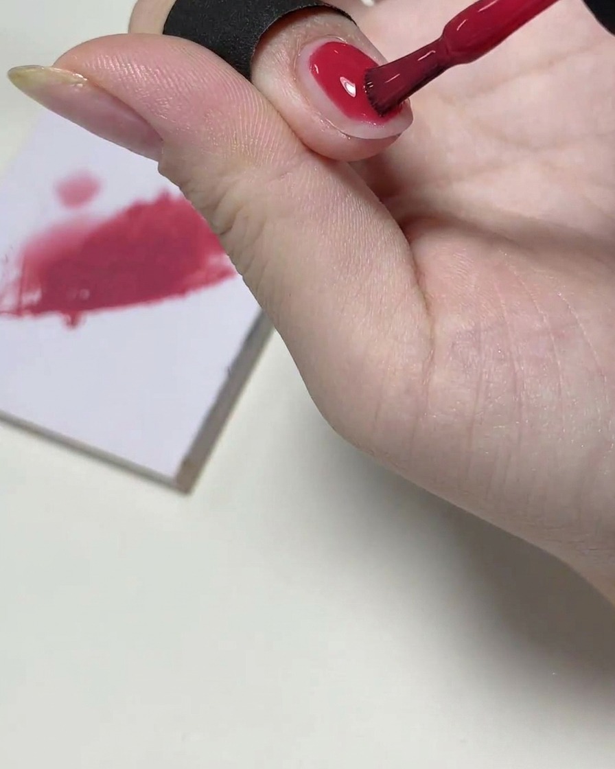 Ein Gelpinsel trägt eine transparente Schicht rosafarbenes Gel auf die obere Hälfte des Nagels auf.