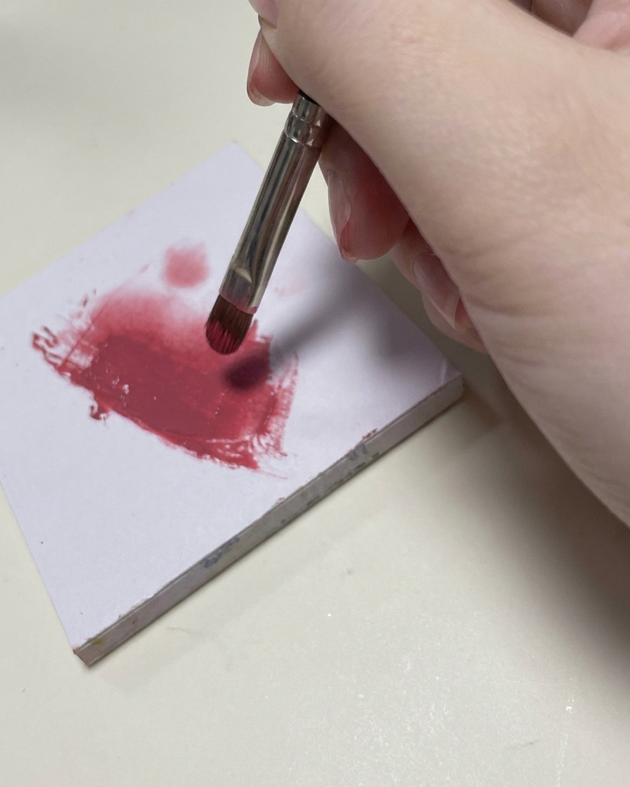 Ein kleiner Nail-Art-Pinsel verblendet rosa Farbgel im mittleren Bereich des Nagels.