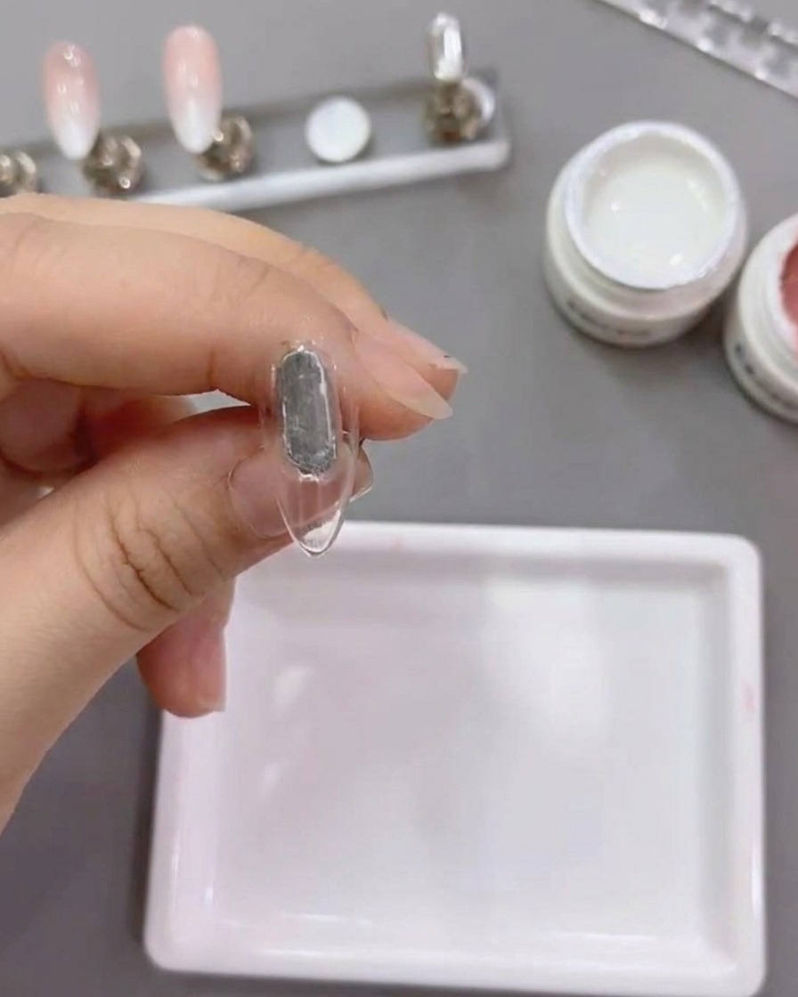 Ein flacher Pinsel trägt weißes Gel der Nummer 79 auf eine natürliche Nagelspitze auf.