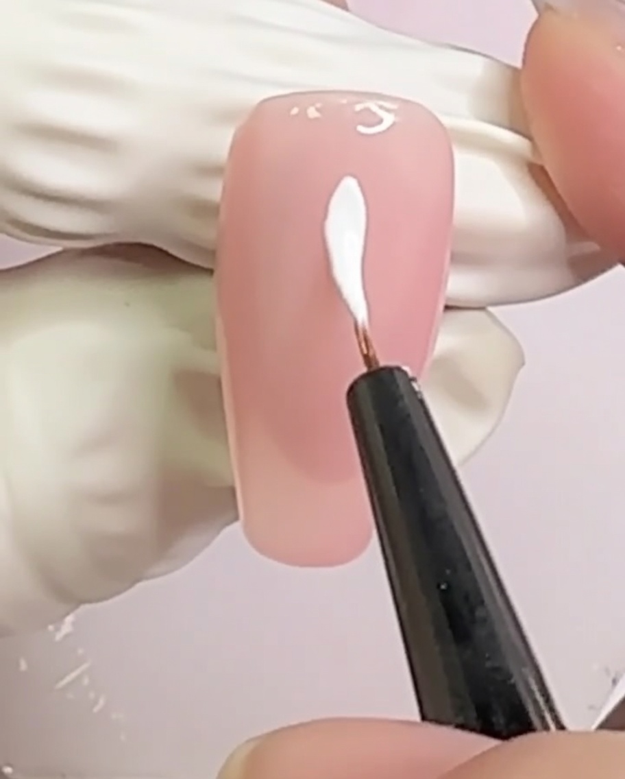 Ein nudefarbener Nagel mit zwei sich in der Mitte kreuzenden weißen Linien in X-Form.