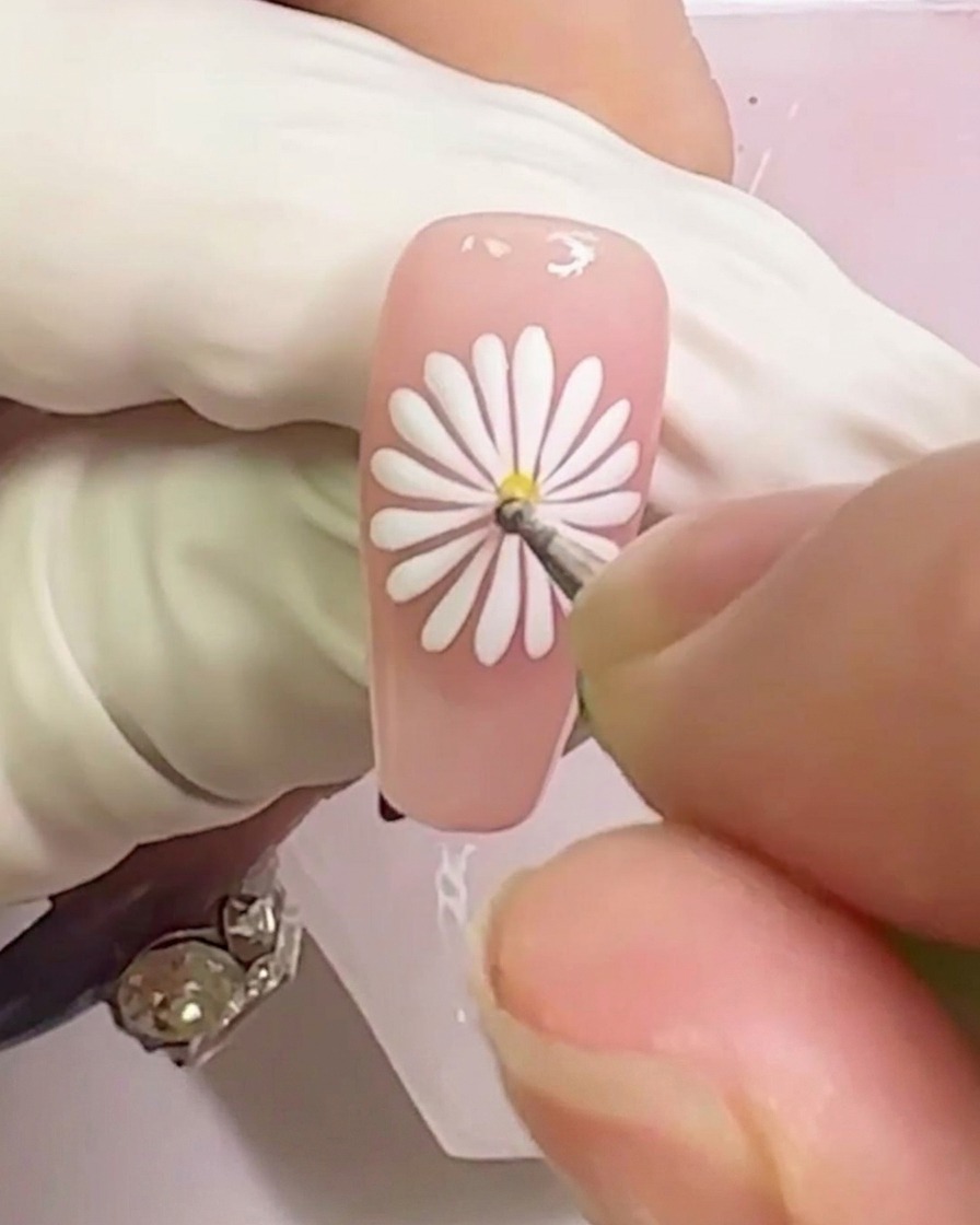 Nahaufnahme, wie ein gelber Gel-Punkt in die Mitte des weißen Gänseblümchen-Designs gesetzt wird.
