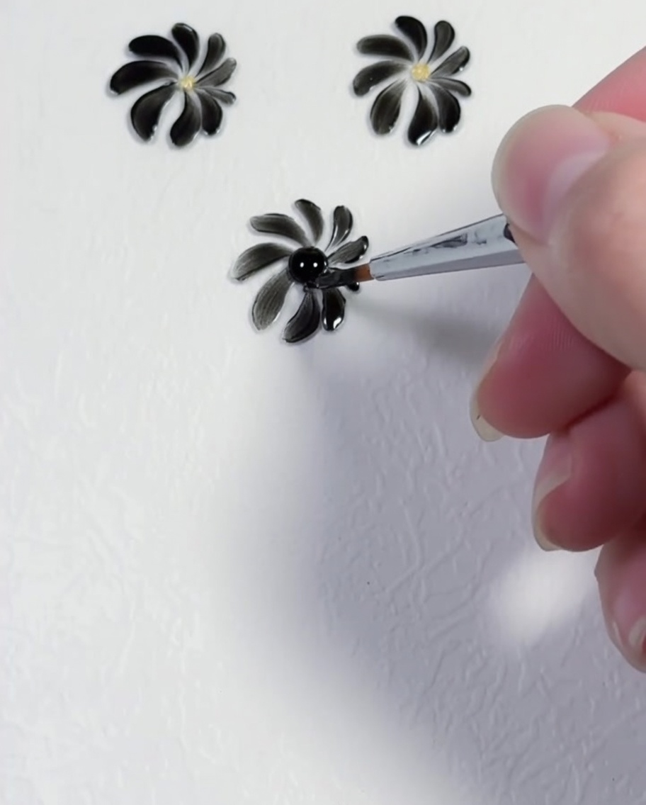 Ein Punktierwerkzeug setzt einen präzisen gelben Punkt in die Mitte eines schwarzen Gänseblümchen-Designs.
