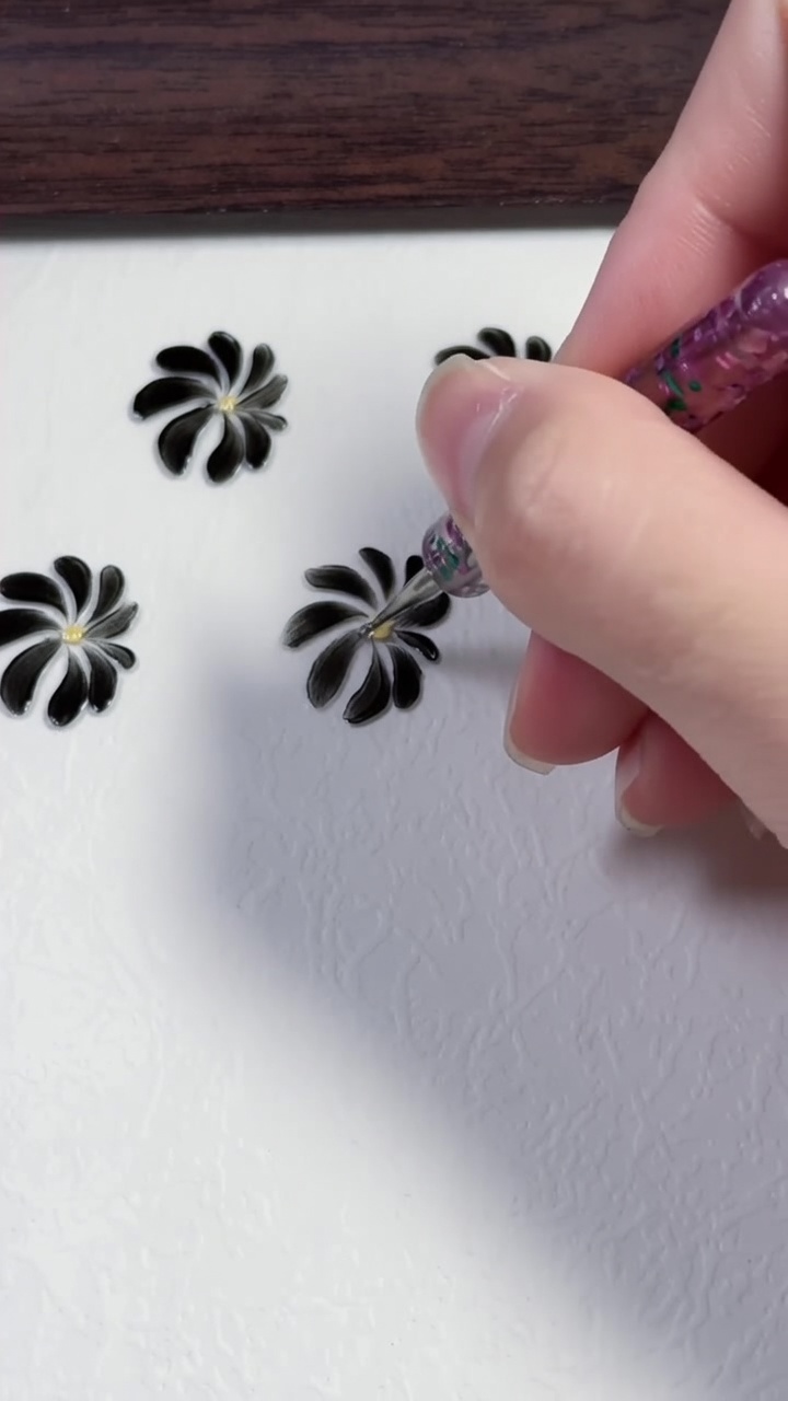 Drei handgemalte schwarze Gänseblümchen mit gelben Zentren auf einer sauberen weißen Oberfläche.
