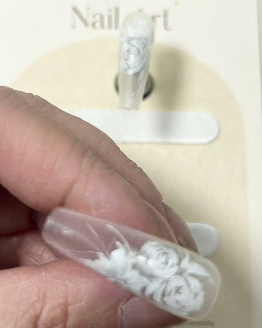 Nahaufnahme eines Nagels mit detailliertem weißen Rosendesign, bei dem der Pinsel letzte zarte weiße Highlights setzt.