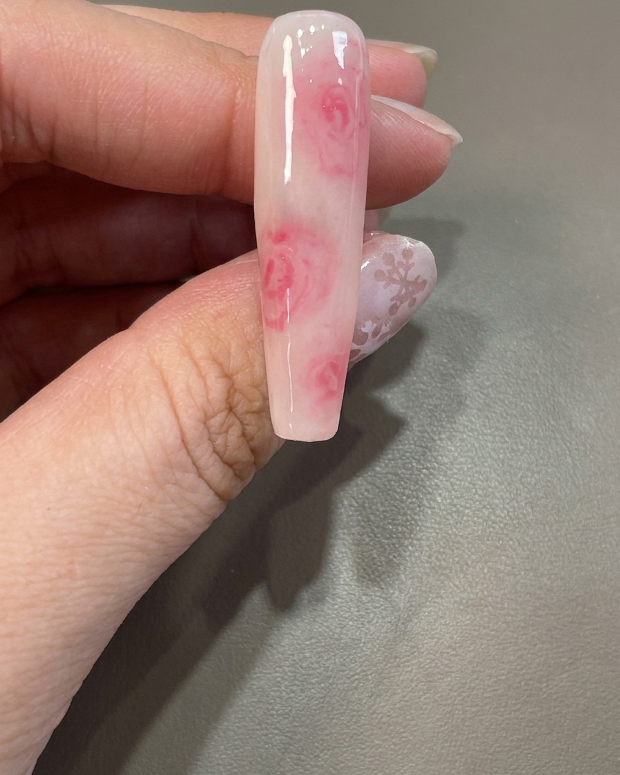 Ein Pinsel trägt eine weitere klare Schicht Blooming Gel über ein bestehendes Nageldesign auf.