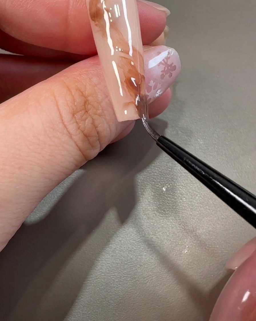 Ein feiner Pinsel zieht durch das braune Gel, um wirbelnde, marmorierte Texturen auf dem Nagel zu erzeugen.