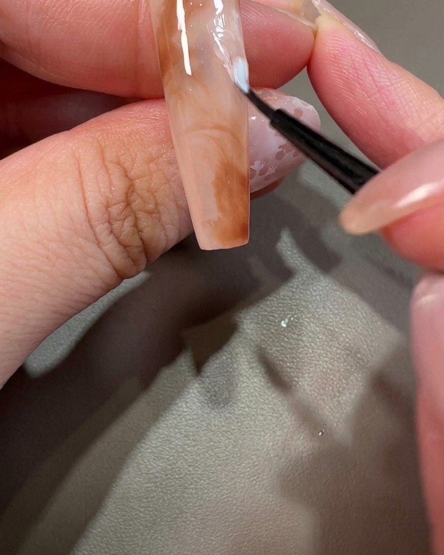 Nahaufnahme eines Nagels, der mit einem winzigen Punkt aus weißem Gel verziert wird.