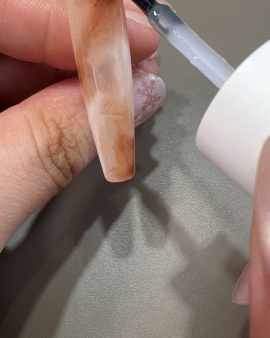 Ein Pinsel trägt klaren Top Coat über ein fertiges Marmor-Nageldesign auf.