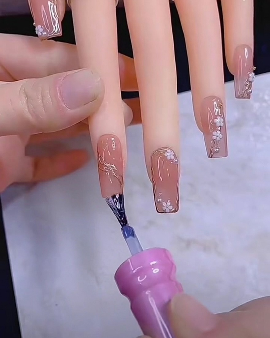 Ein Dotting-Tool platziert kleine weiße Blütenblätter auf einem Gelnagel.