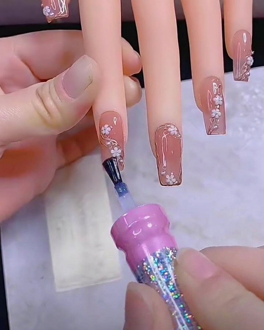 Ein Pinsel trägt eine letzte, glatte Schicht des glänzenden Top Coats auf einen fertig dekorierten Nagel auf.