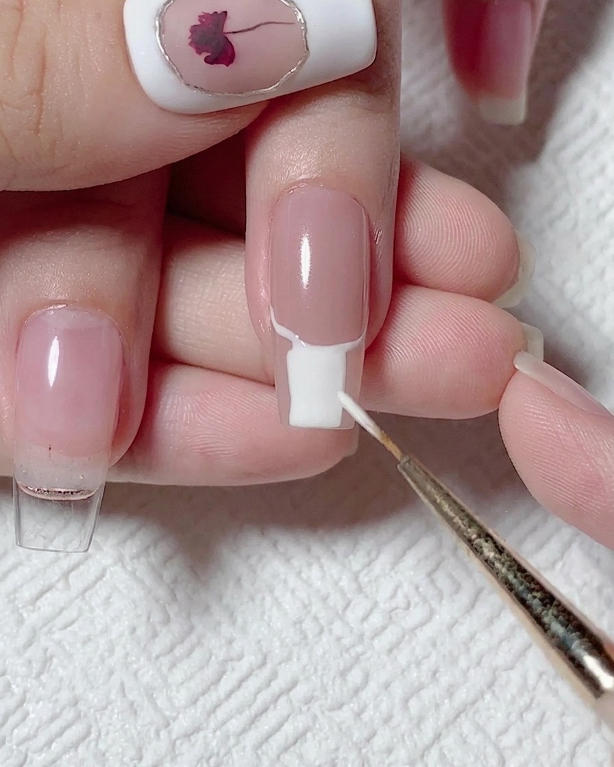 Ein flacher Pinsel füllt den unteren Bereich eines Nagels mit deckendem, weißem Gel-Nagellack aus.