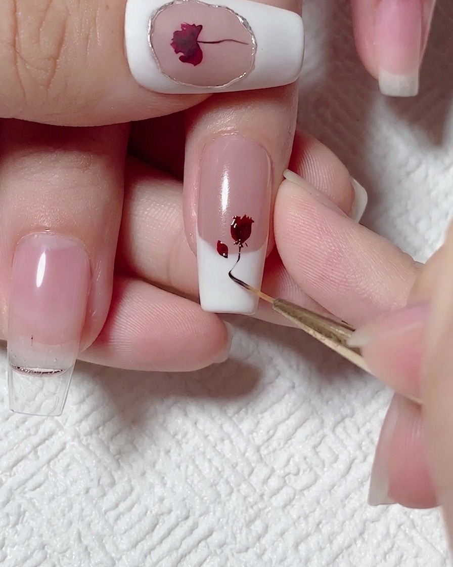 Ein Liner-Pinsel zieht eine dünne, geschwungene Linie aus schwarz-braunem Gel von einer roten Rose auf einem Nagel abwärts.