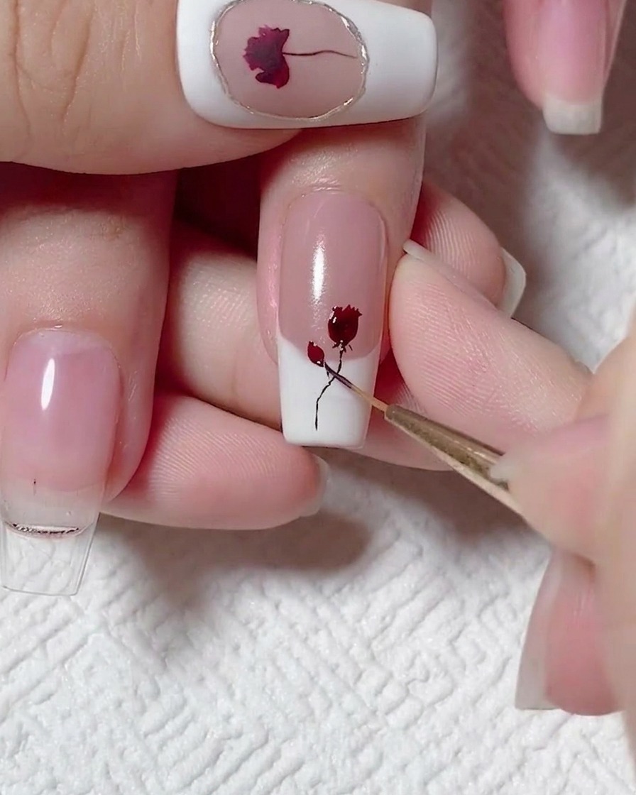 Ein feiner Liner-Pinsel fügt winzige dunkle Blätter zu einem gemalten schwarzen Stiel und Rosen-Design auf einem Nagel hinzu.
