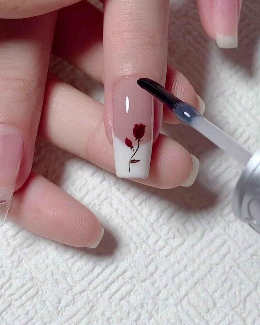 Ein Gel-Pinsel aus einem Fläschchen trägt eine glatte, klare Schicht Verstärkungsgel über ein gemaltes Rosen-Design auf.