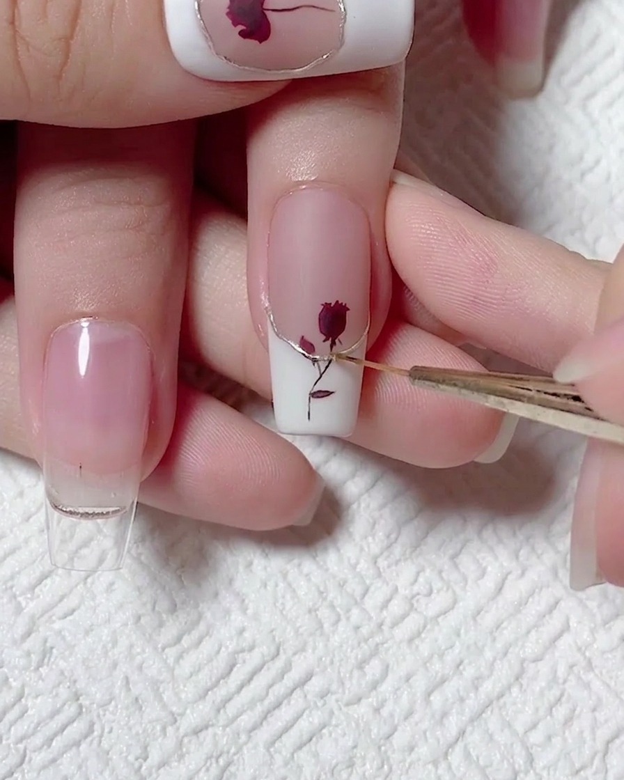 Nahaufnahme, wie ein feiner Liner-Pinsel eine präzise Linie Top Coat über einen metallischen champagnergoldenen Akzent auf einem weißen French-Nagel aufträgt.