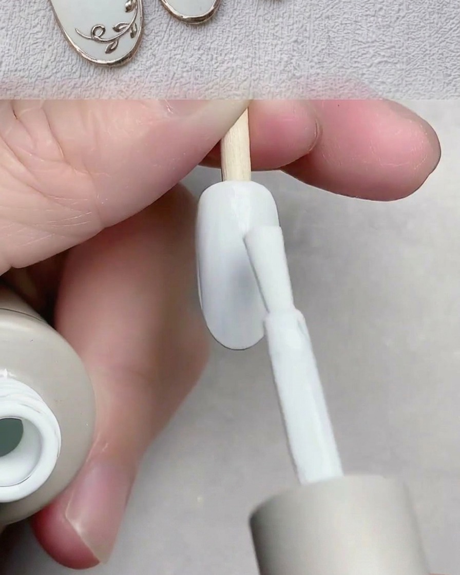 Ein Pinsel trägt glattes weißes Gel auf eine Nagelspitze auf.