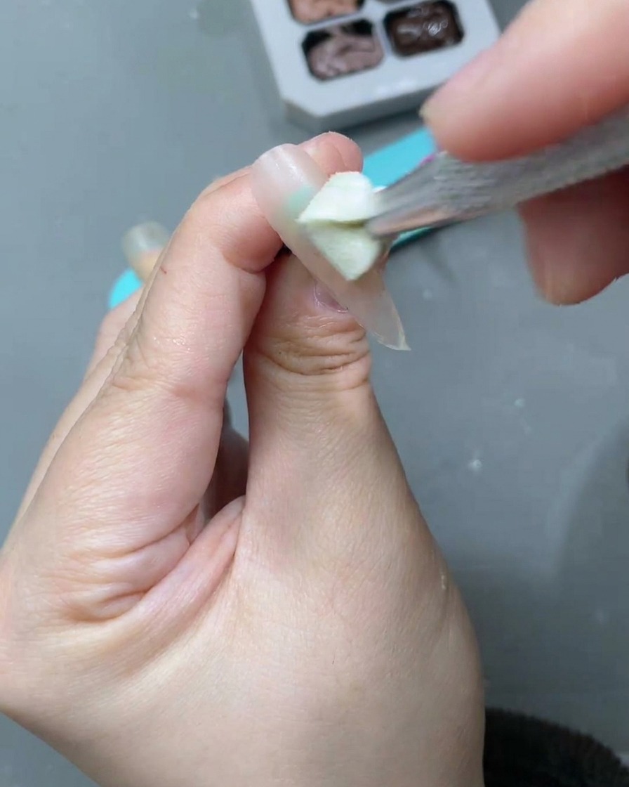 Ein Nagelpinsel verteilt ein weißes Moon-Cat-Eye-Gel über der Nude-Basis.