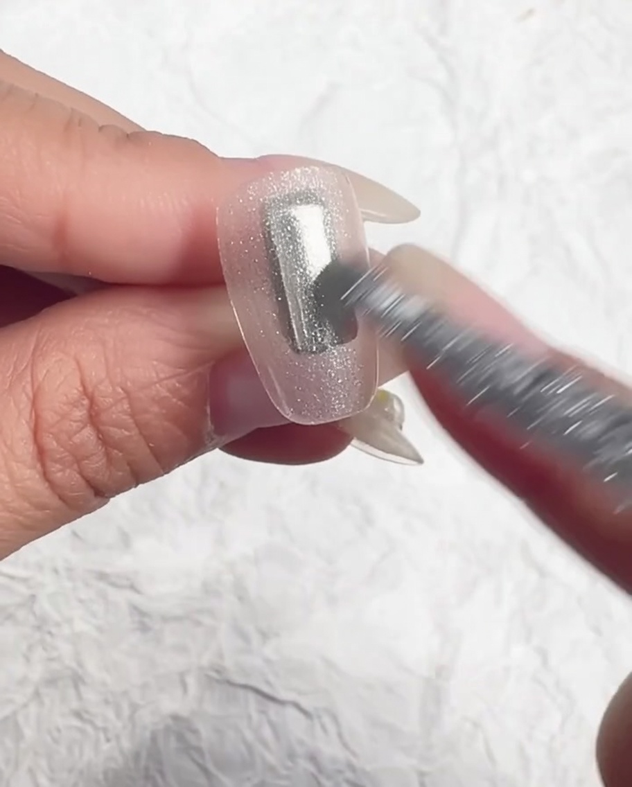 Ein Pinsel gleicht das eis-transluzente Gel auf dem Nagel aus.