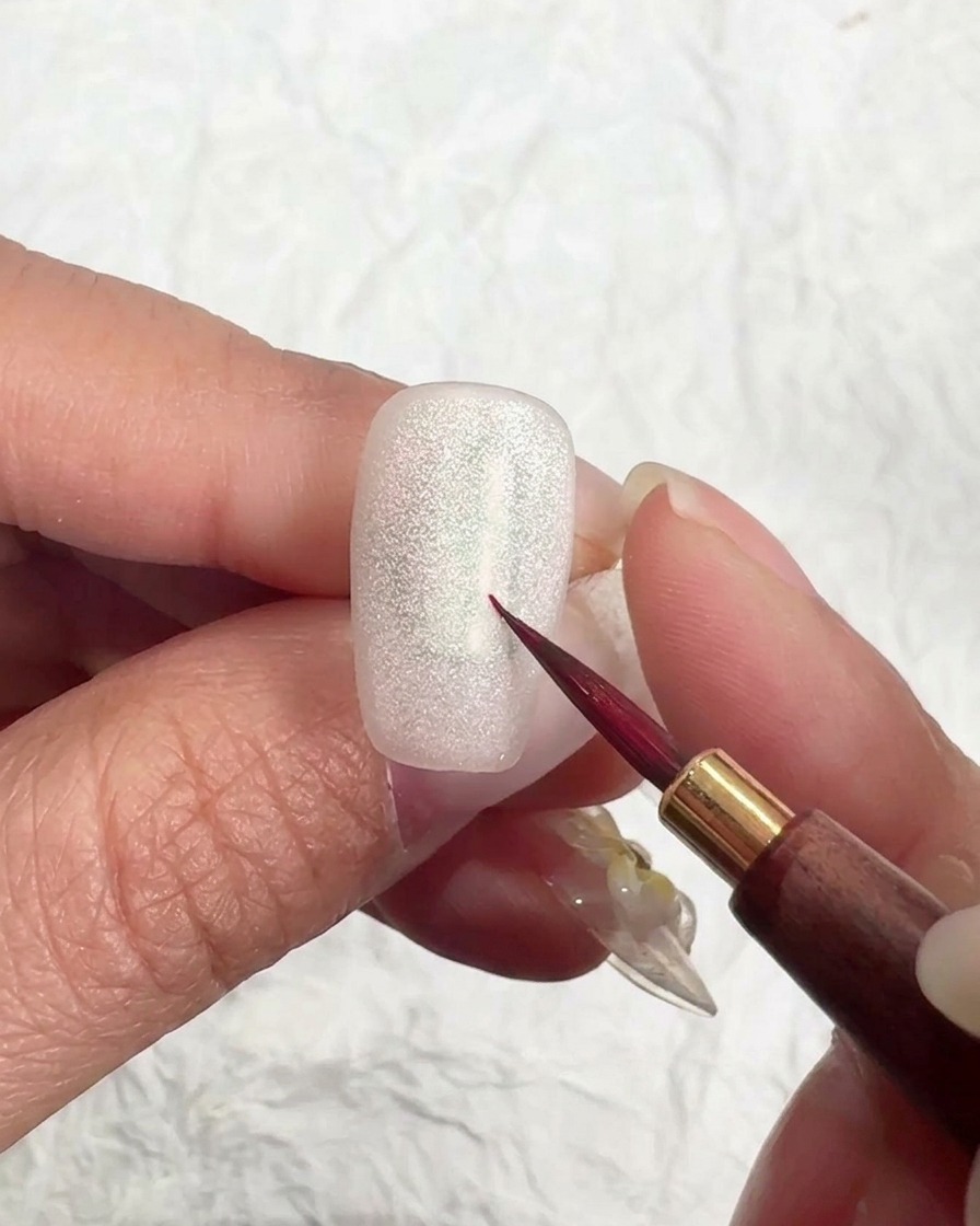 Ein Pinsel trägt ein mattes Top Gel über einen schimmernden Cat-Eye-Nagel auf.
