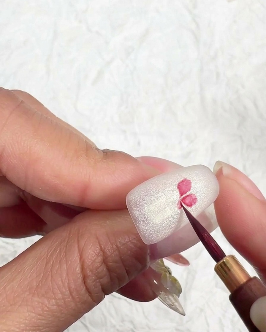 Ein feiner Nailart-Pinsel zeichnet das Zentrum einer rosa Kirschblüte auf einer matten Nageloberfläche.