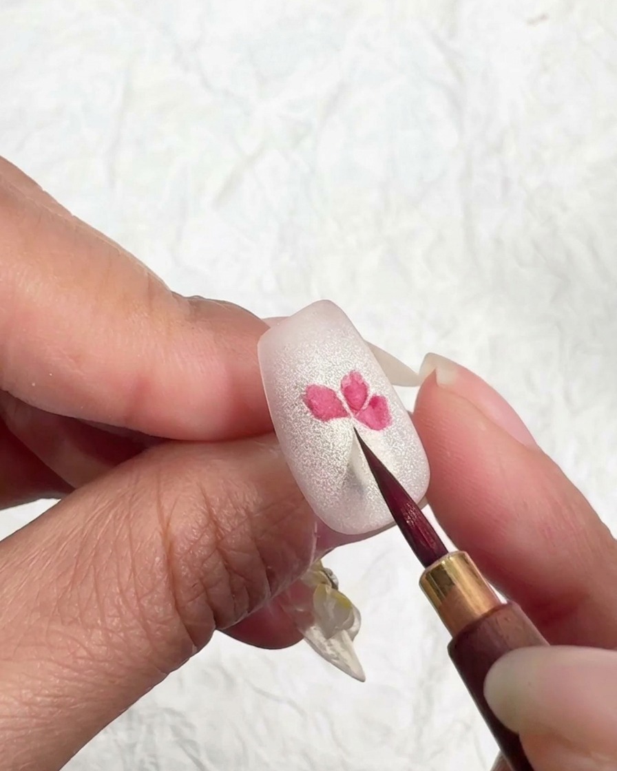 Ein feiner Pinsel berührt leicht die Ränder eines rosa Blütenblatts, um die Farbe aufzuweichen.