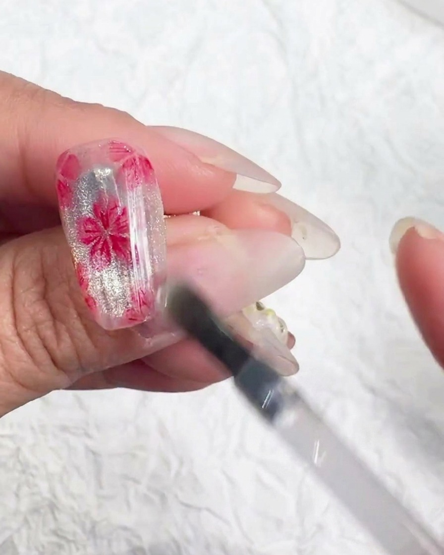 Ein Nailart-Werkzeug platziert winzige schillernde Flocken in der Mitte einer Kirschblüte.