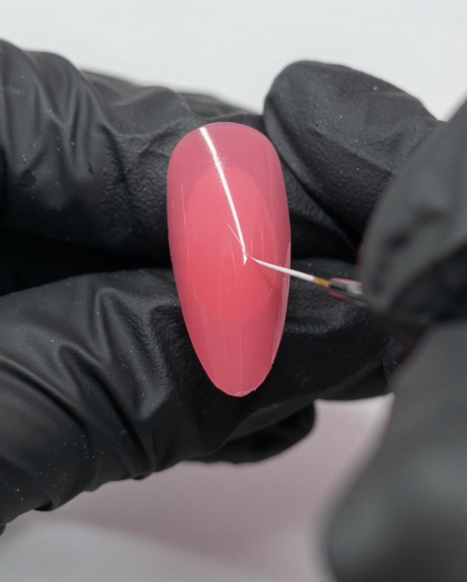 Nahaufnahme eines pinkfarbenen Nagels mit einem kleinen weißen Punkt und einer feinen Linie, die mit einem Liner-Pinsel gezeichnet wurde.