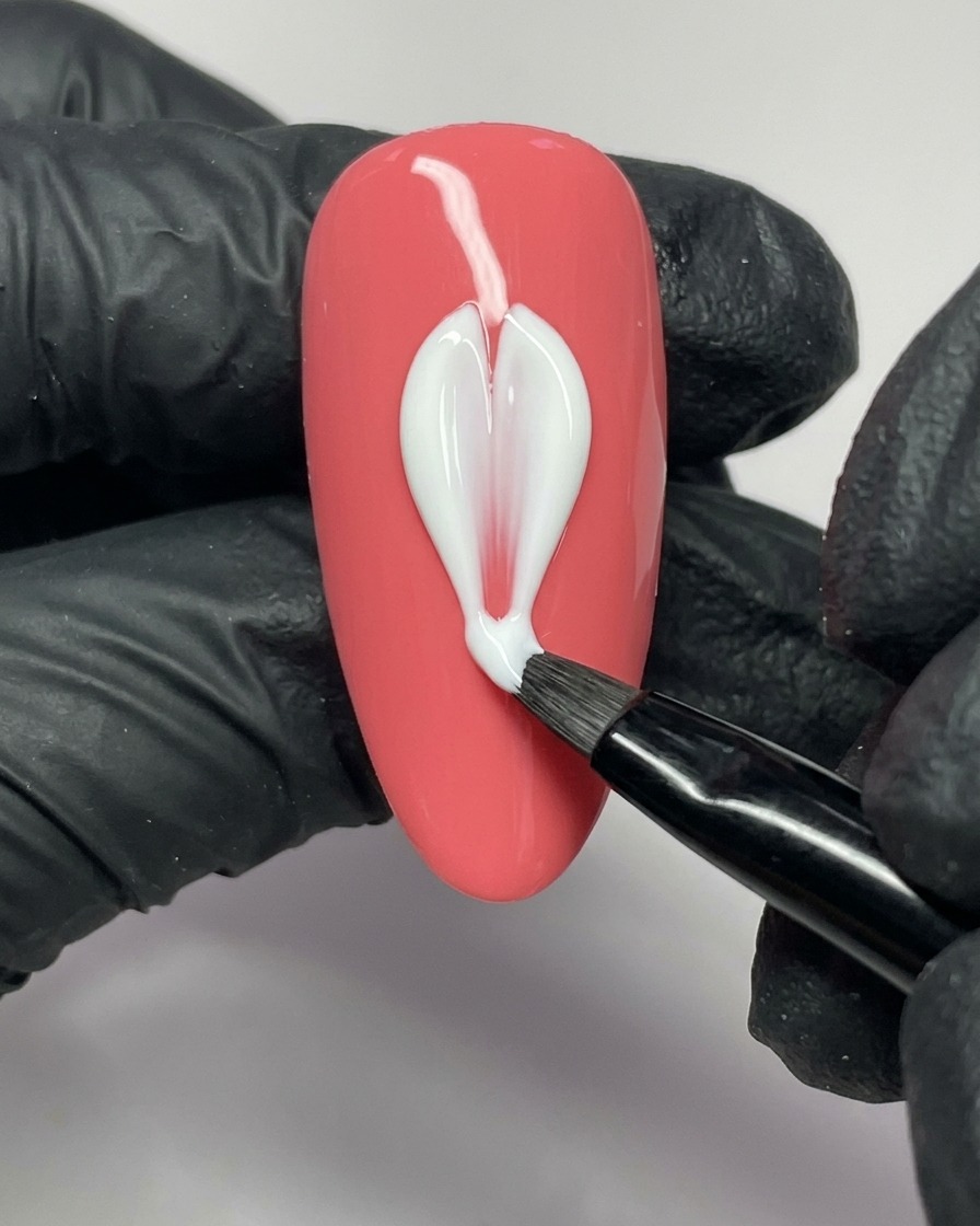 Ein Nagelkunstpinsel trägt weißes Gel auf, um die linke Seite eines Blütenblattes auf einem pinkfarbenen Nagel zu formen.