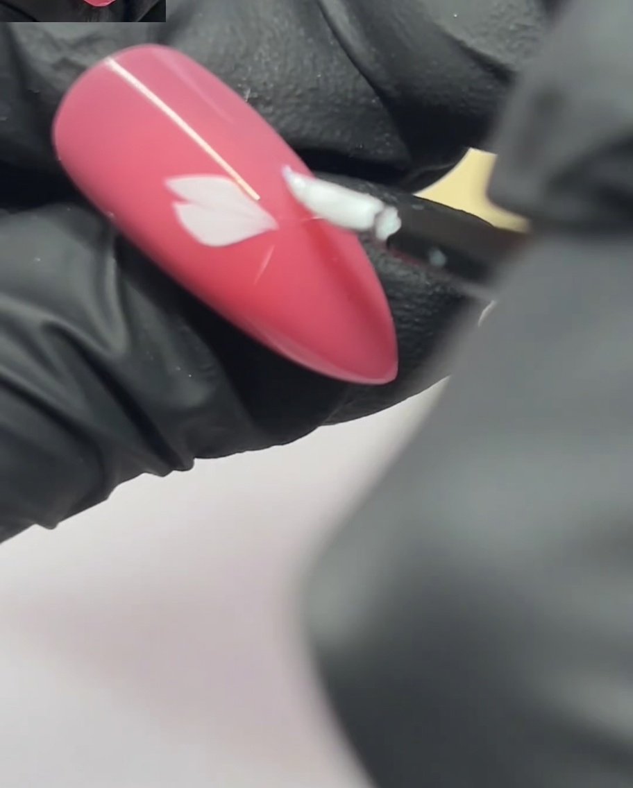 Ein Nagelkunstpinsel trägt ein zweites Blütenblatt neben dem ersten auf einem pinkfarbenen Nagel auf.