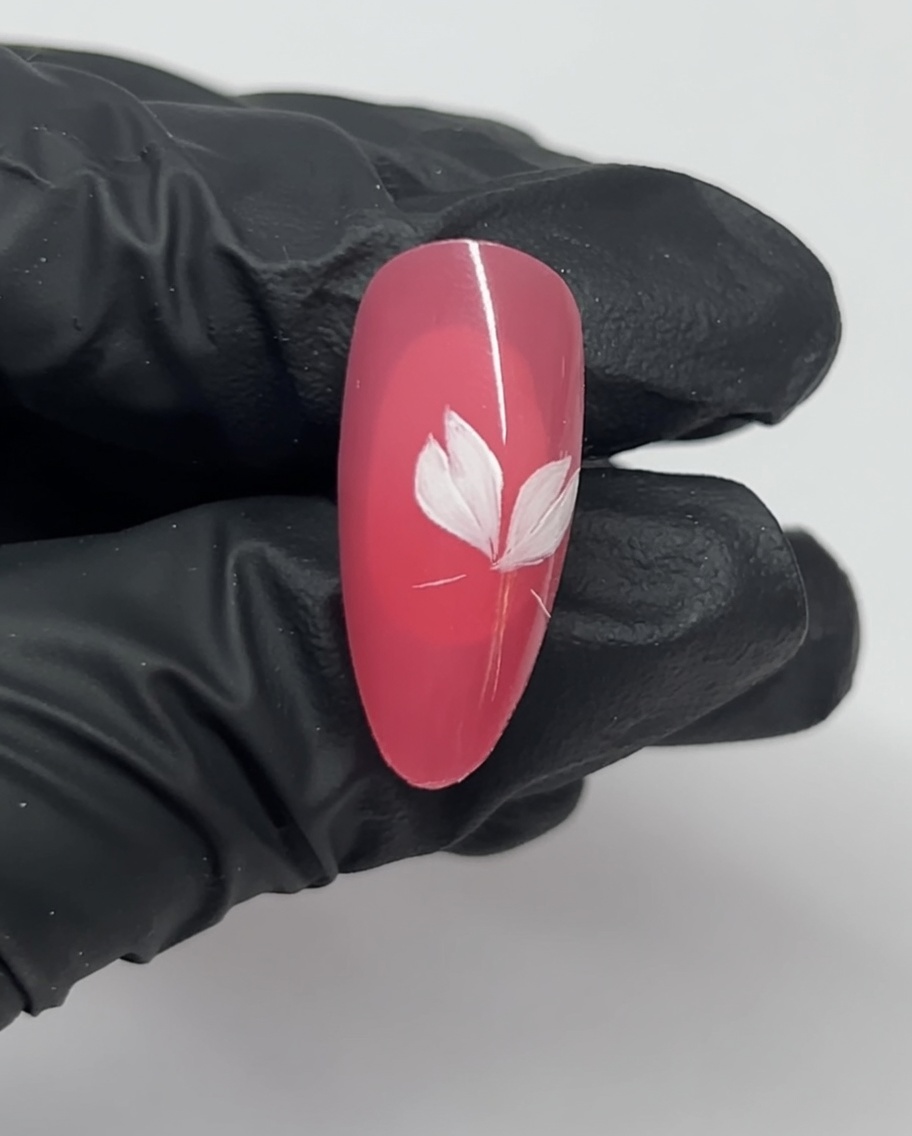 Nahaufnahme eines Nagels mit drei weißen Blütenblättern eines Kirschblüten-Designs auf pinkfarbenem Untergrund.