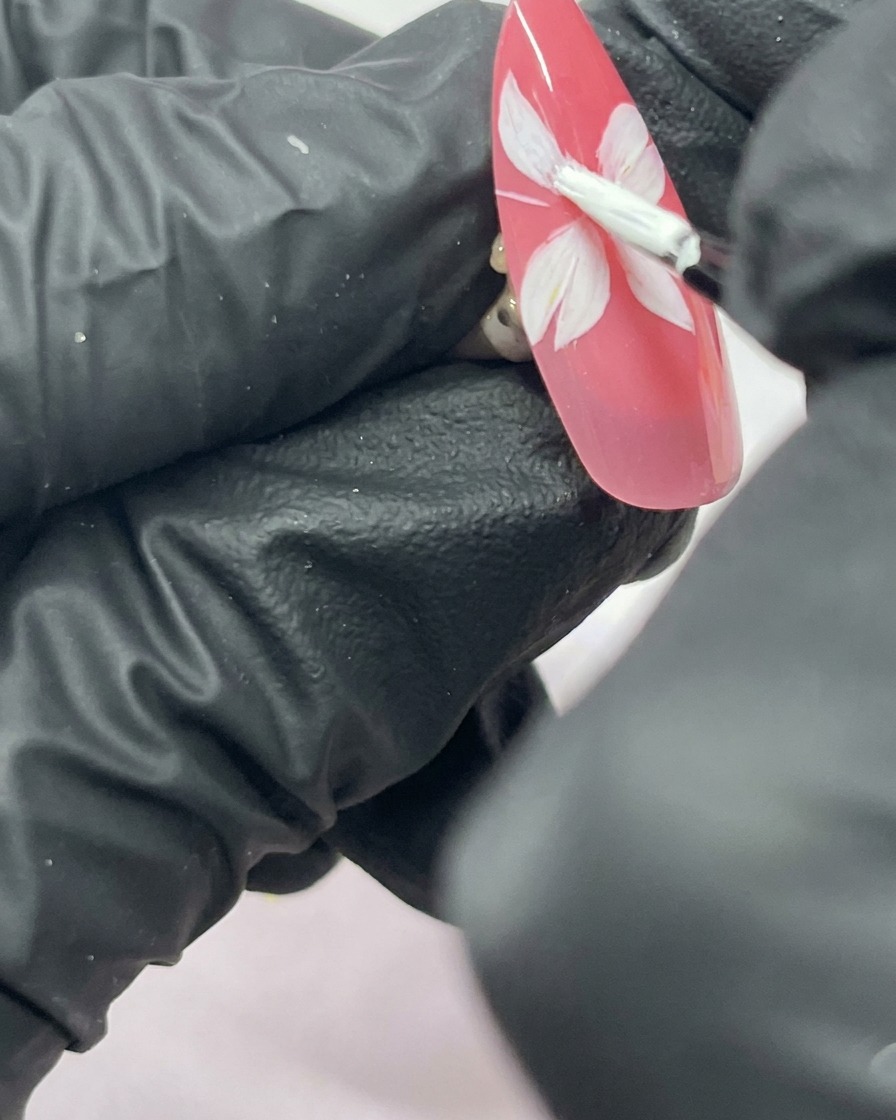Nahaufnahme eines Nagels mit einer fünfblättrigen weißen Kirschblüte auf einem pinkfarbenen Hintergrund.
