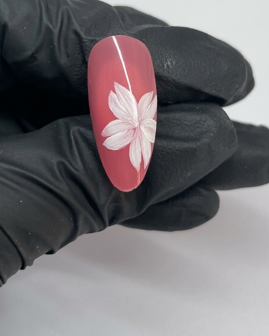 Nahaufnahme eines fertigen Kirschblüten-Nageldesigns mit einer vollständigen Blüte und einem weißen Stempelzentrum.