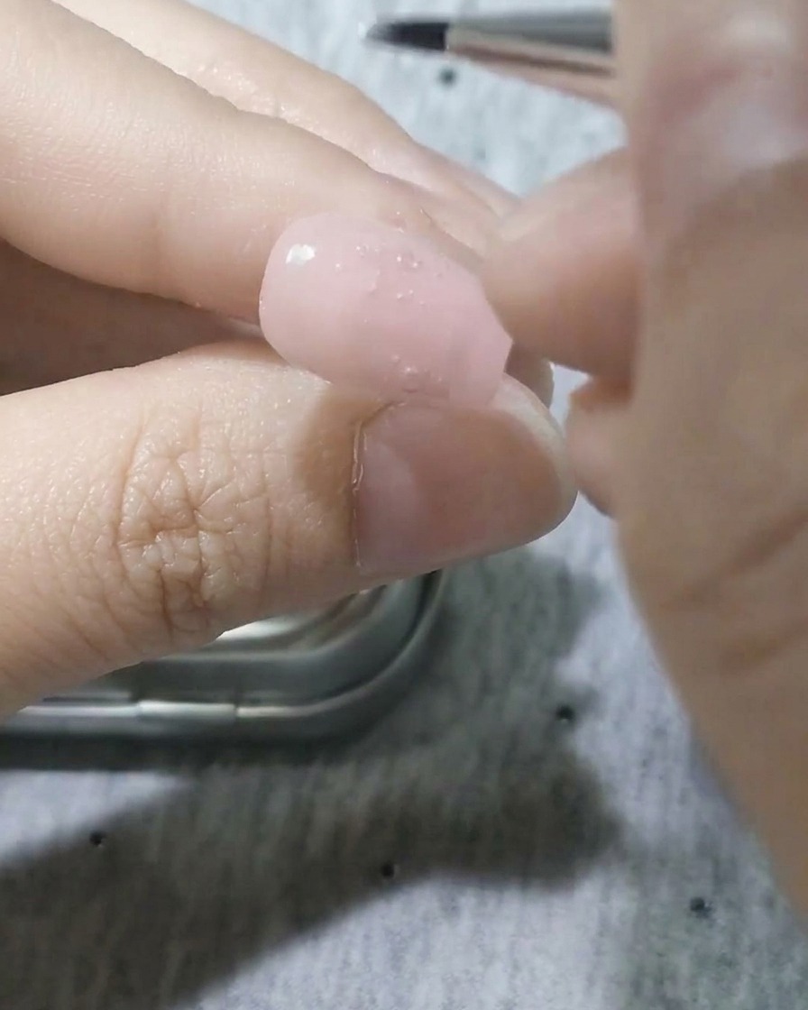 Ein feiner Detailpinsel trägt weißes Gel auf, um eine Blütenblattform auf dem Nagel zu bilden.