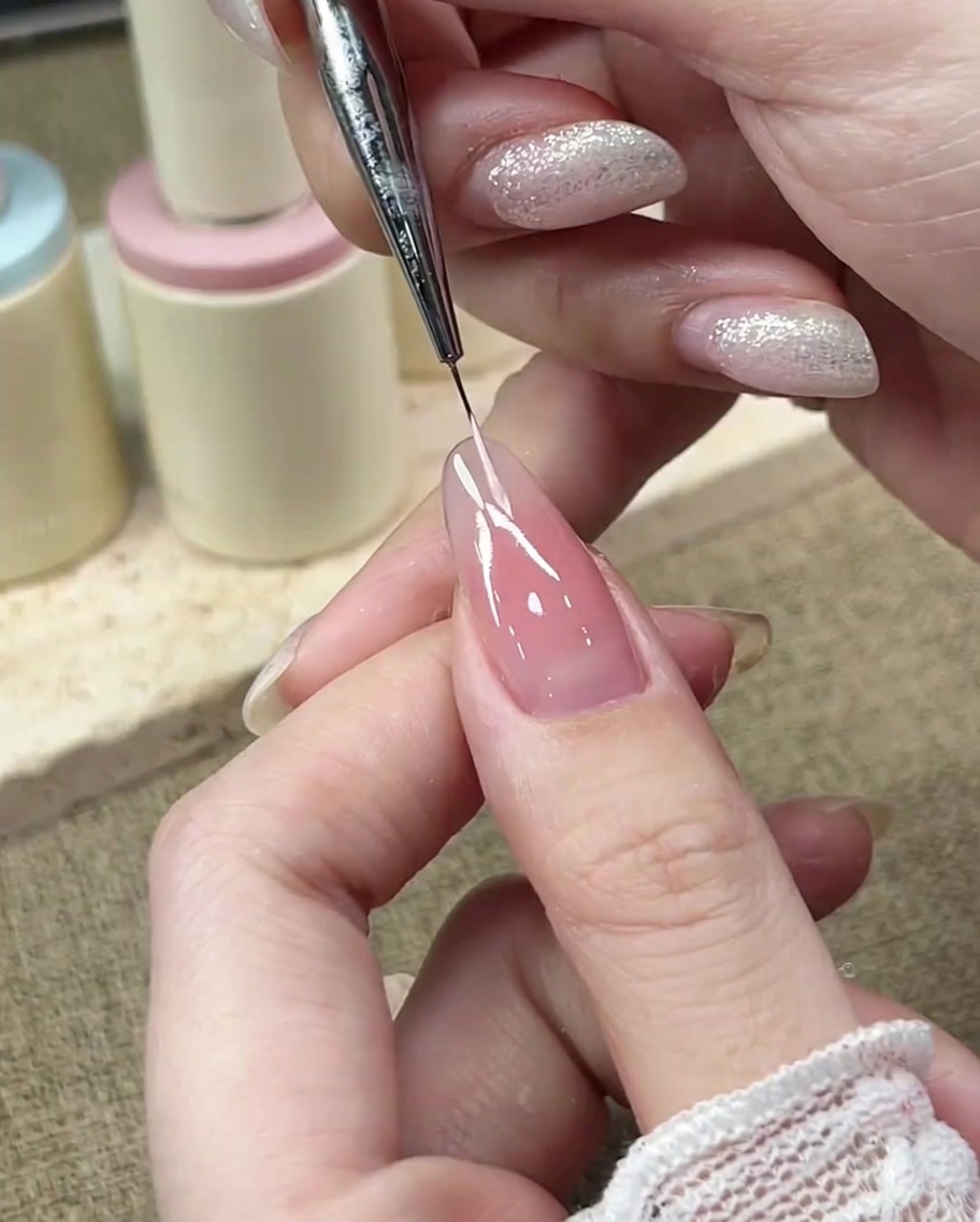 Ein feiner Detailpinsel zeichnet die linke Kurve einer French-Smile-Line mit pastellrosa Gel.