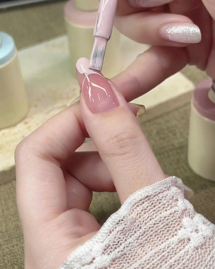 Ein Nagelpinsel füllt den French-Spitzenbereich mit pastellrosa Gel-Polish aus.