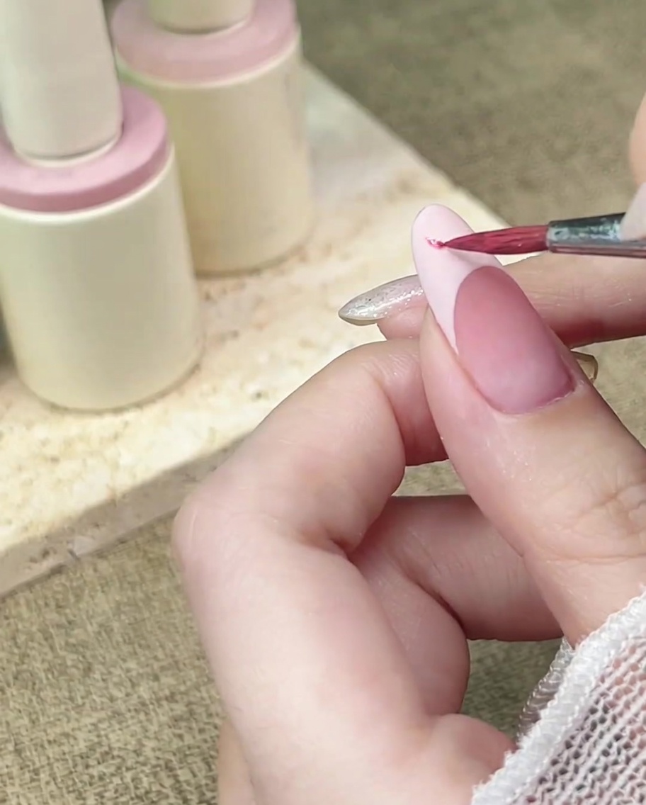 Ein Detailpinsel tupft rosa Aquarellfarbe auf eine mattierte French-Spitze.
