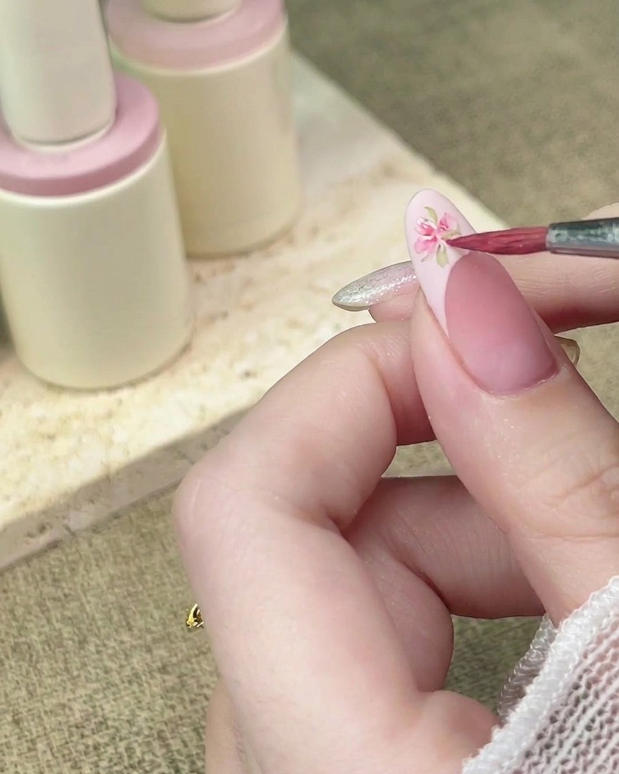 Ein Detailpinsel fügt weitere rosa Aquarell-Blütenblätter hinzu, um ein florales Design auf einer French-Spitze zu vervollständigen.