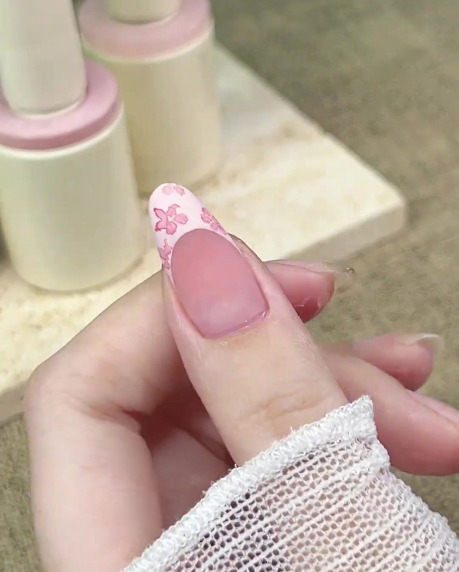 Eine Nahaufnahme zeigt einen Detailpinsel, der einen konzentrierten Punkt dunklerer rosa Farbe in die Mitte eines floralen Designs setzt.