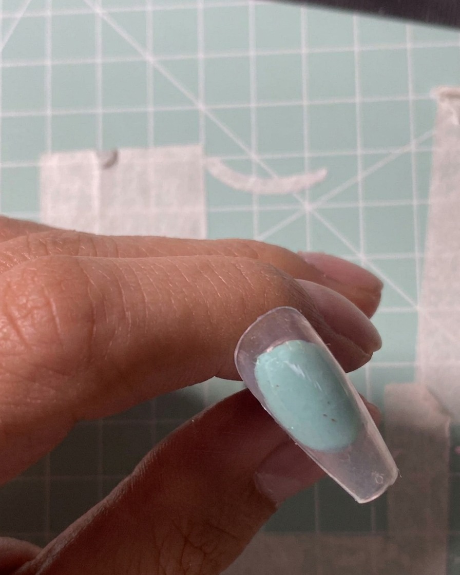 Nahaufnahme eines elektrischen Fräseraufsatzes, der die Oberfläche eines klaren Nageltips anraut.