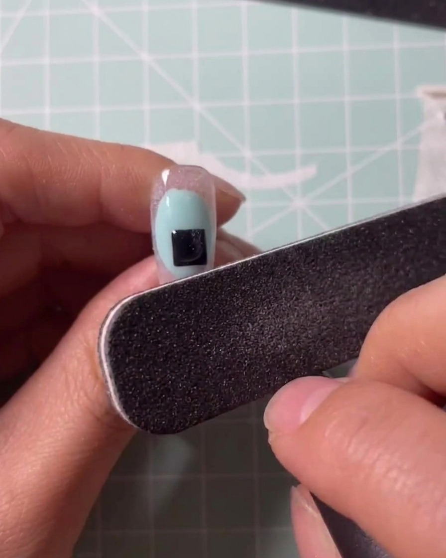 Ein Pinsel trägt klares Gel auf einen durchsichtigen Nagelverlängerungstip auf.