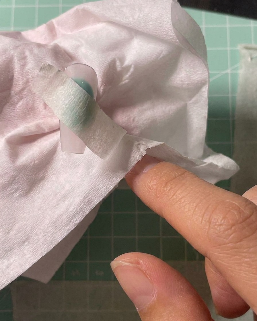 Airbrush-Pistole sprüht weiße Pigmentfarbe auf die Mitte eines mit Schablone abgeklebten Nageltips.