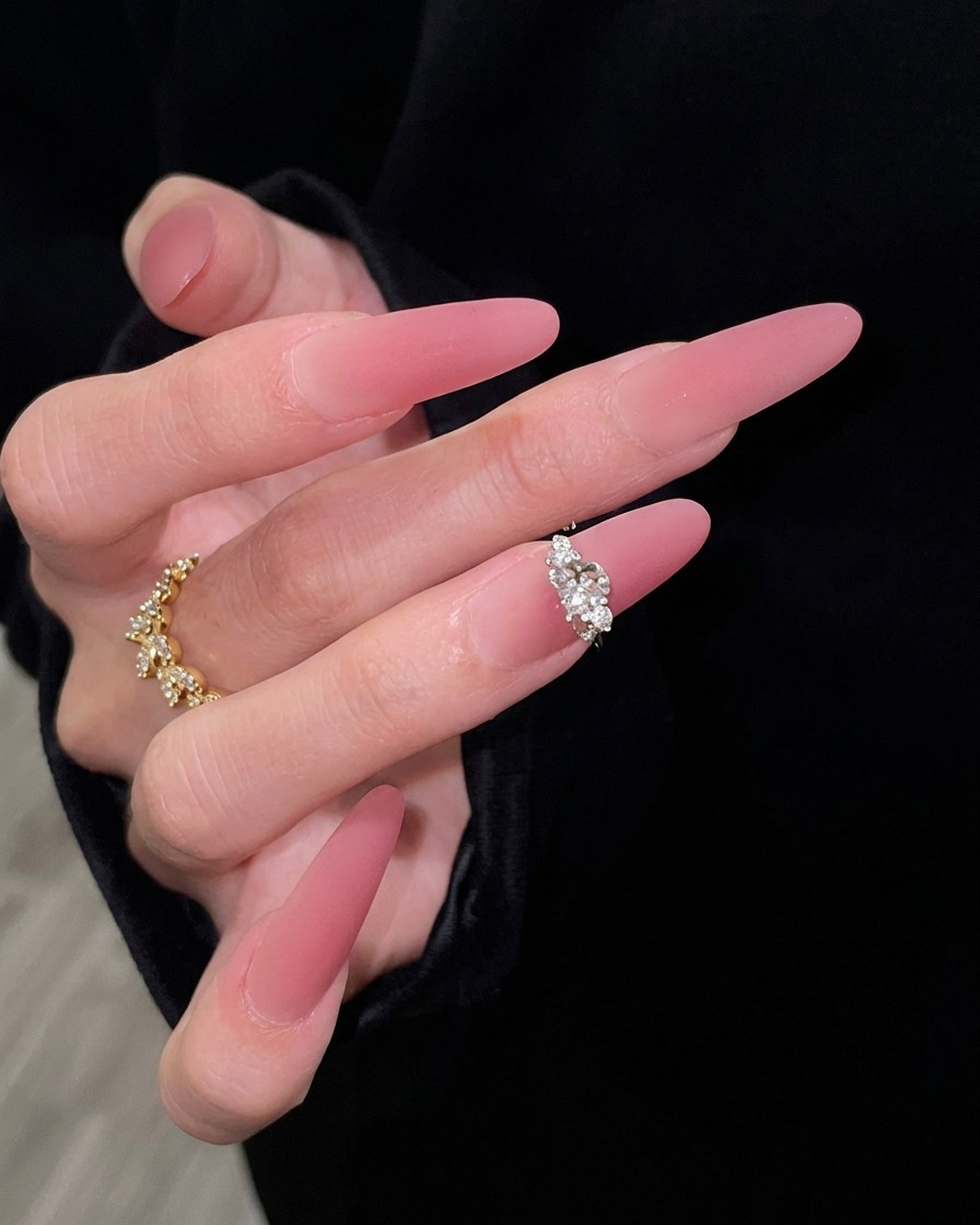 Eine Hand mit langen, rosafarbenen Gradienten-Nägeln, elegant vor einem schwarzen Ärmelhintergrund posiert, um den nahtlosen Übergang von transparentem Nude zu dunklem Rosé zu betonen.