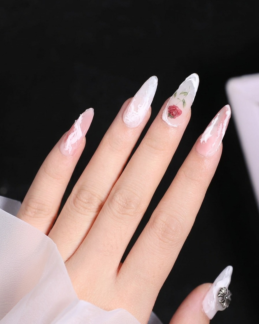 Nahaufnahme eines Nagels mit einer gemalten Rose, bei dem ein kleiner Pinsel die Basis eines grünen Blattes neben der Blume ergänzt.