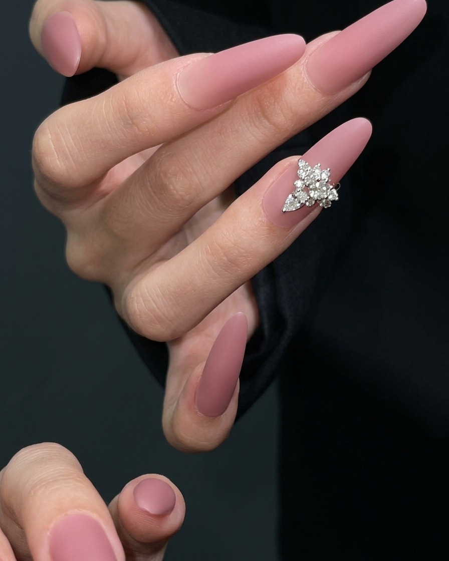 Ein Nail-Art-Pinsel, der eine Schicht matten Top Coat auf einen getrockneten mauvefarbenen Nagel aufträgt.