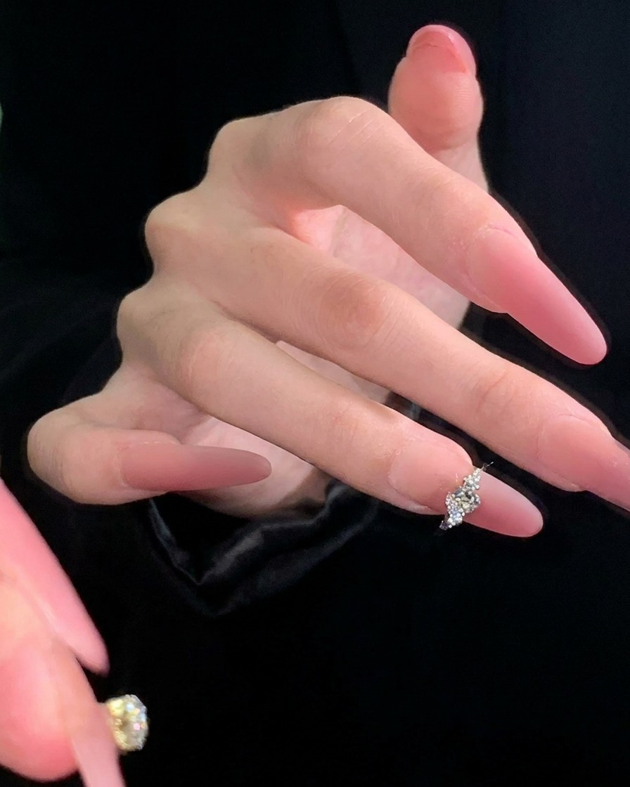 Eine Pinzette, die vorsichtig einen kleinen silbernen Charm in Schmetterlingsform auf der Mitte eines mauvefarbenen Nagels positioniert.