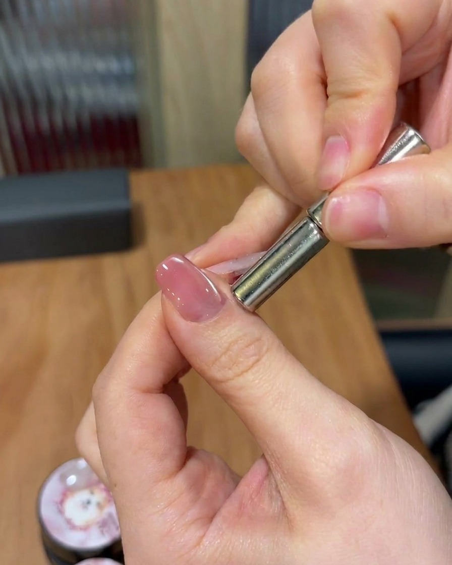 Eine Hand hält einen zylindrischen Magneten über einen Nagel und bewegt ihn, um die magnetischen Partikel zu einem schimmernden diagonalen Band zu formen.