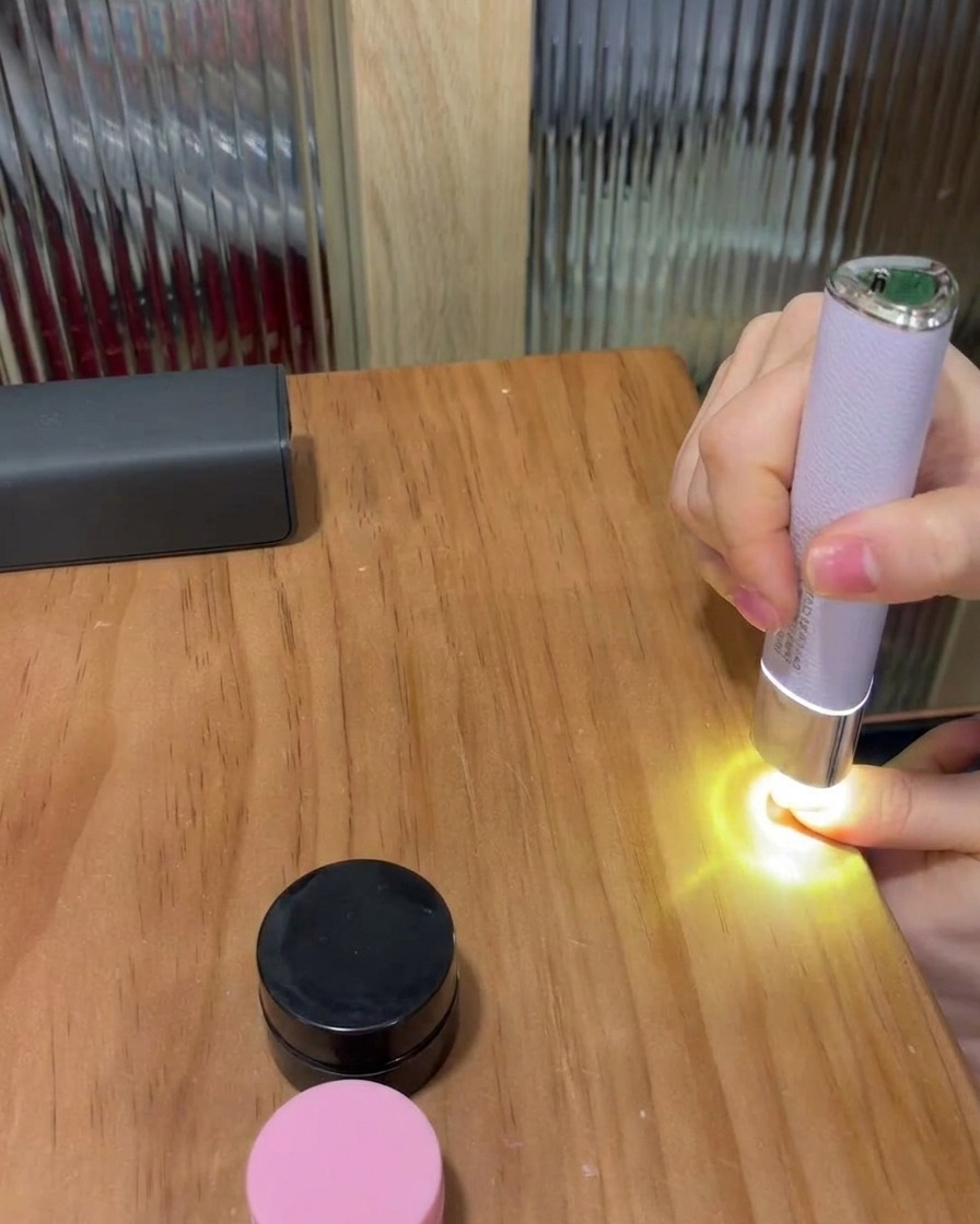 Ein Fingernagel unter einer kleinen, tragbaren violetten LED-Lampe auf einem Holztisch beim Aushärten des Gels.