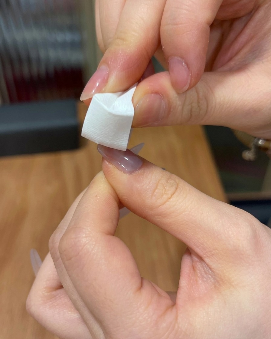 Nahaufnahme eines weißen Schwammkeils, der benutzt wird, um rosa Gel auf die Spitze eines Nagels zu tupfen.