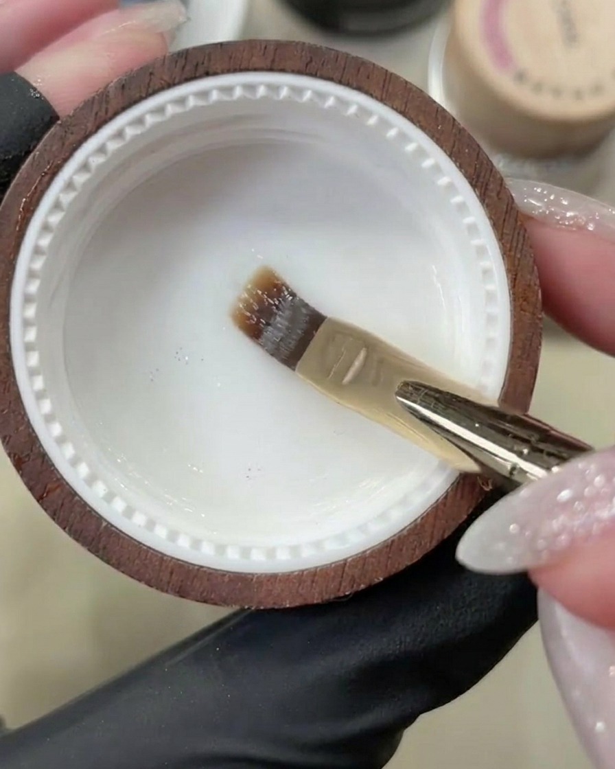 Ein Gelpinsel trägt einen klaren Base Coat auf einen sauberen, natürlichen Fingernagel auf.