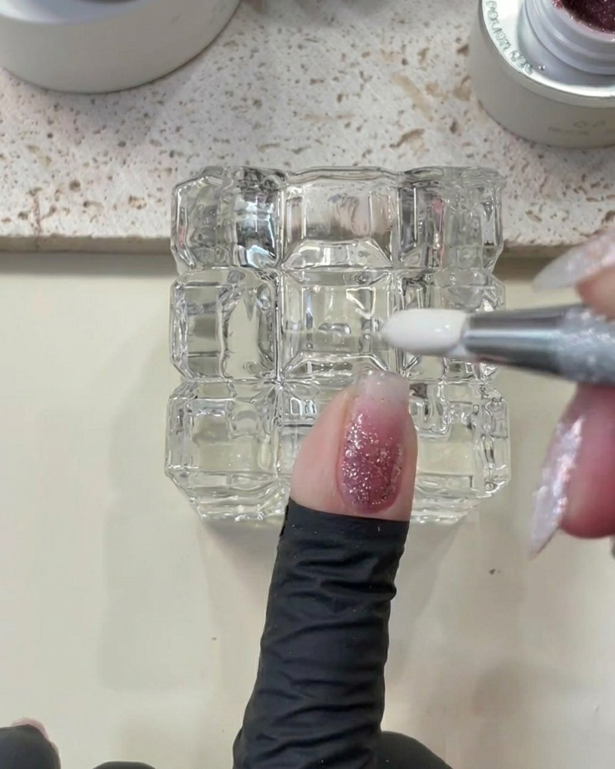 Ein Metallwerkzeug wird verwendet, um überschüssiges Gel um den Nagelhautbereich eines Fingernagels zu entfernen.
